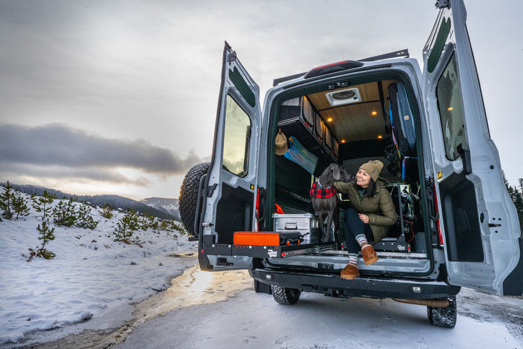 Woman with dog sitting at the back of an open van in the snow