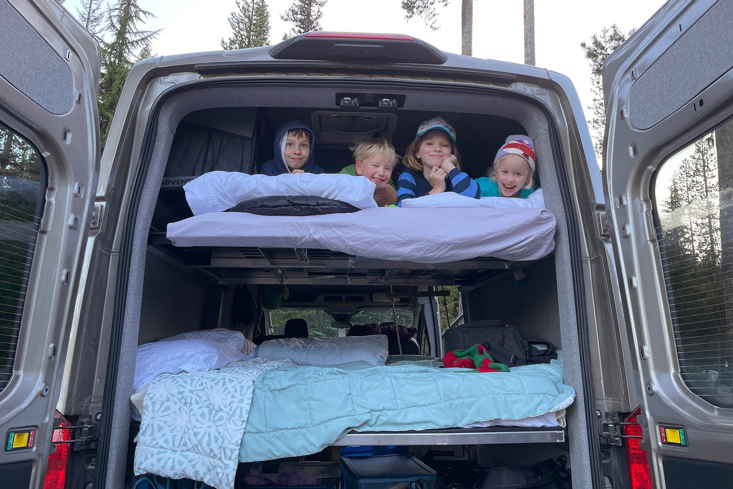 Children smiling from the back of a van on adjustable camper van bed.