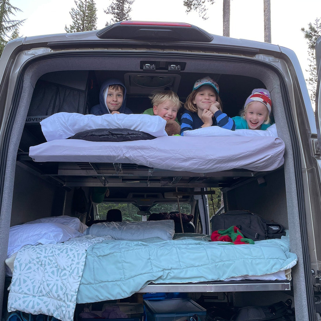 Children smiling from the back of a van on adjustable camper van bed.