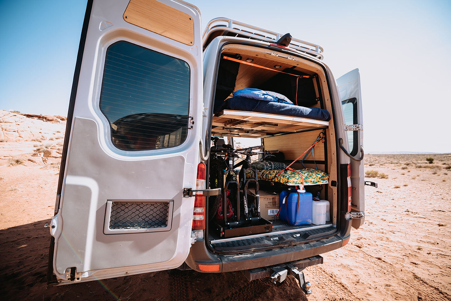 Van in desert area with back doors open to reveal adjustable van bed system