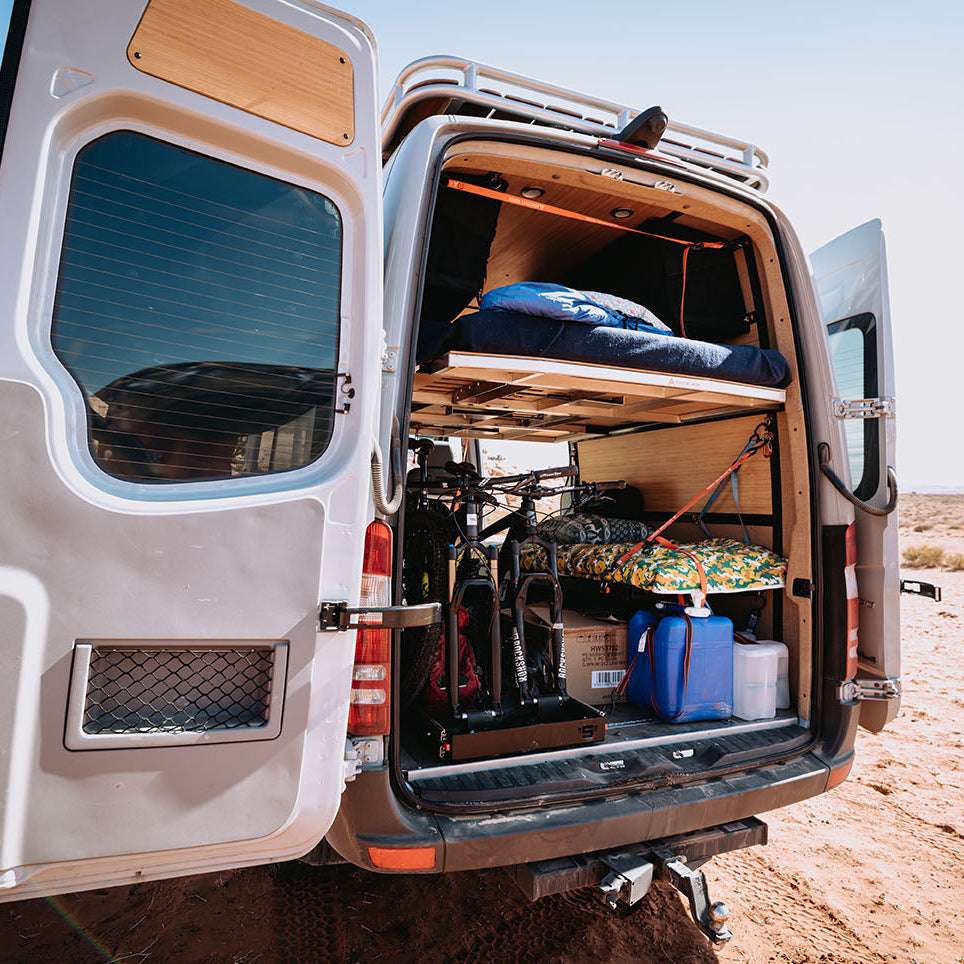 Van in desert area with back doors open to reveal adjustable van bed system