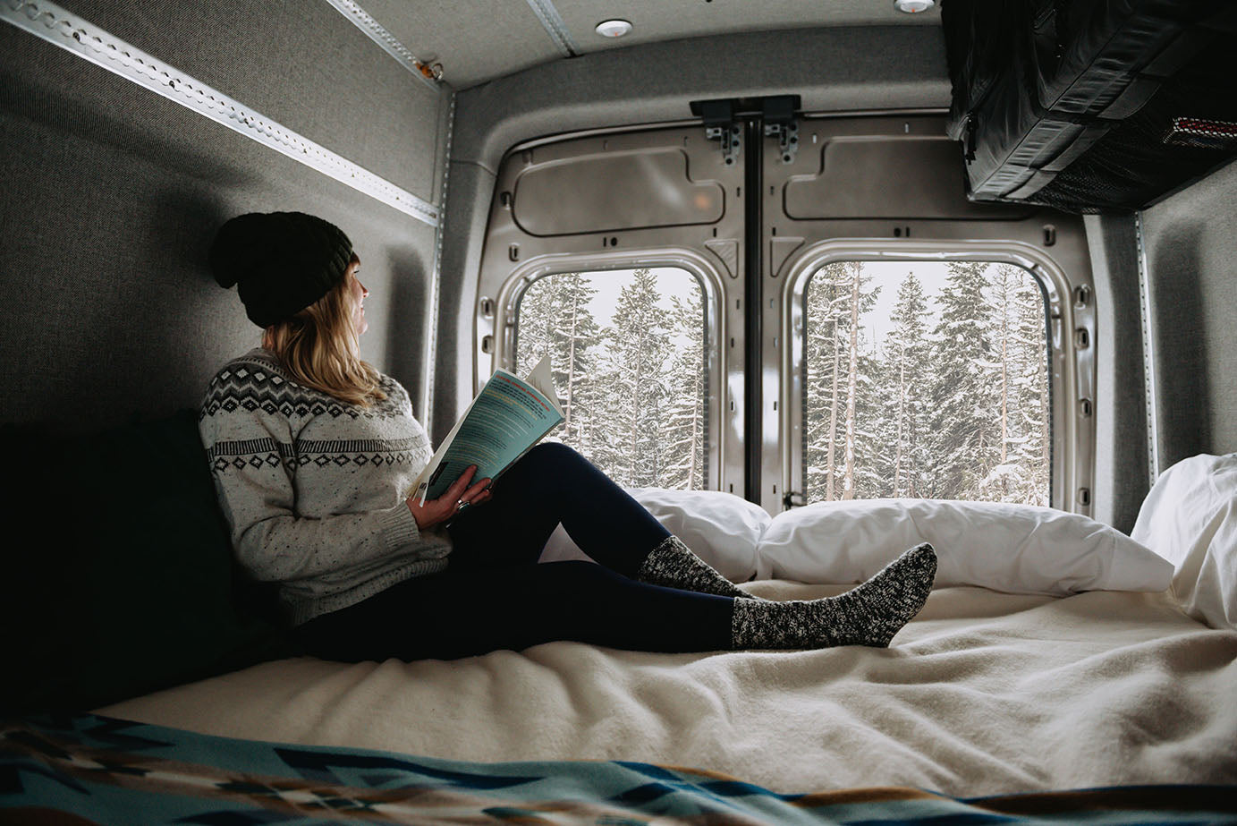 Woman lounging on adjustable van bed during winter