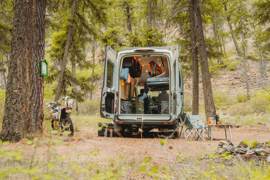 Adventure Wagon Solo Nomad camper van parked at a forest campsite with rear doors open.
