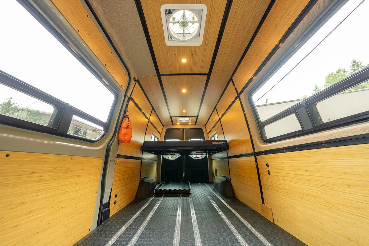 Adventure Wagon camper van interior with bamboo wall and ceiling panels, integrated L-Track and a raised modular bed platform.