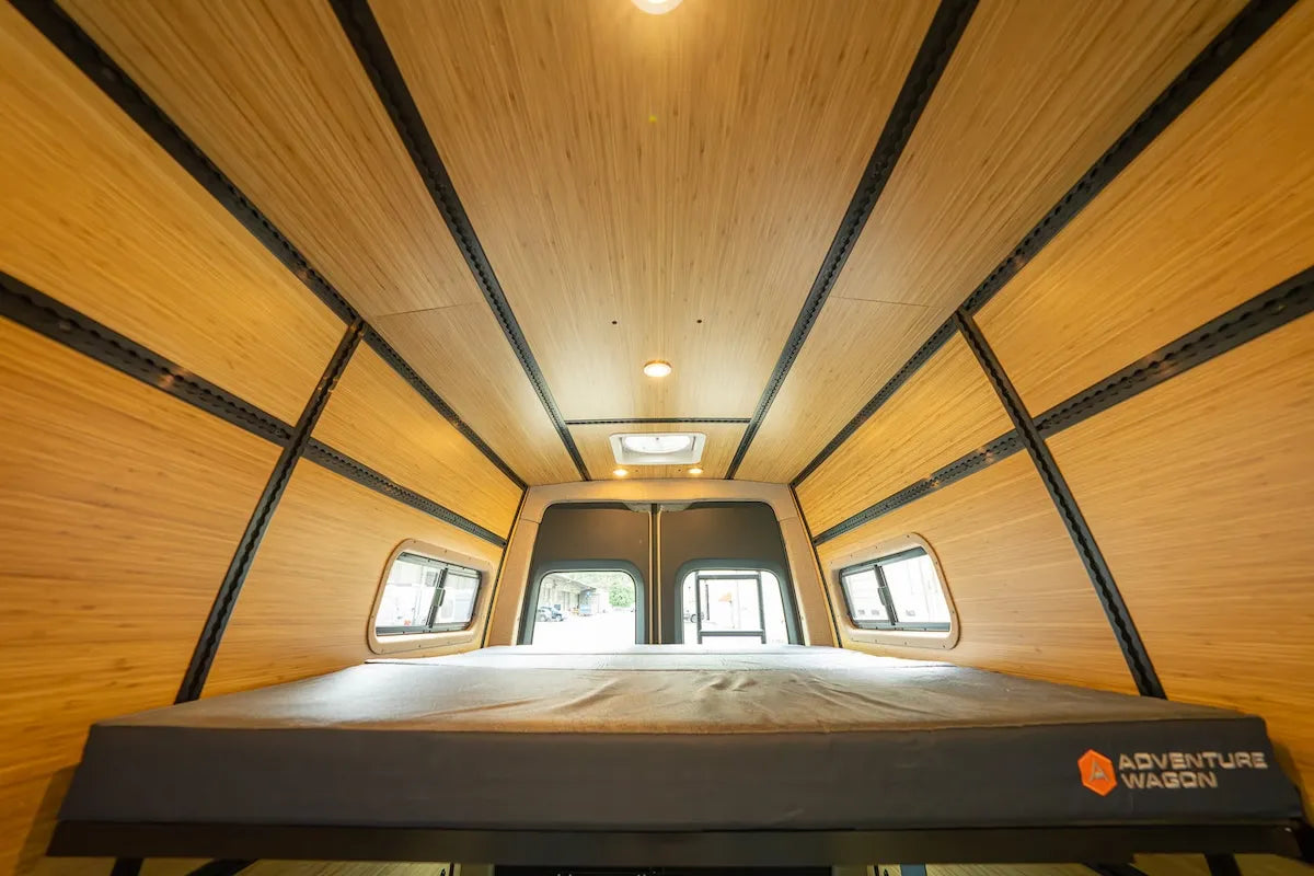 Adventure Wagon camper van interior featuring warm bamboo wall and ceiling panels, integrated L-Track and a raised modular bed platform.