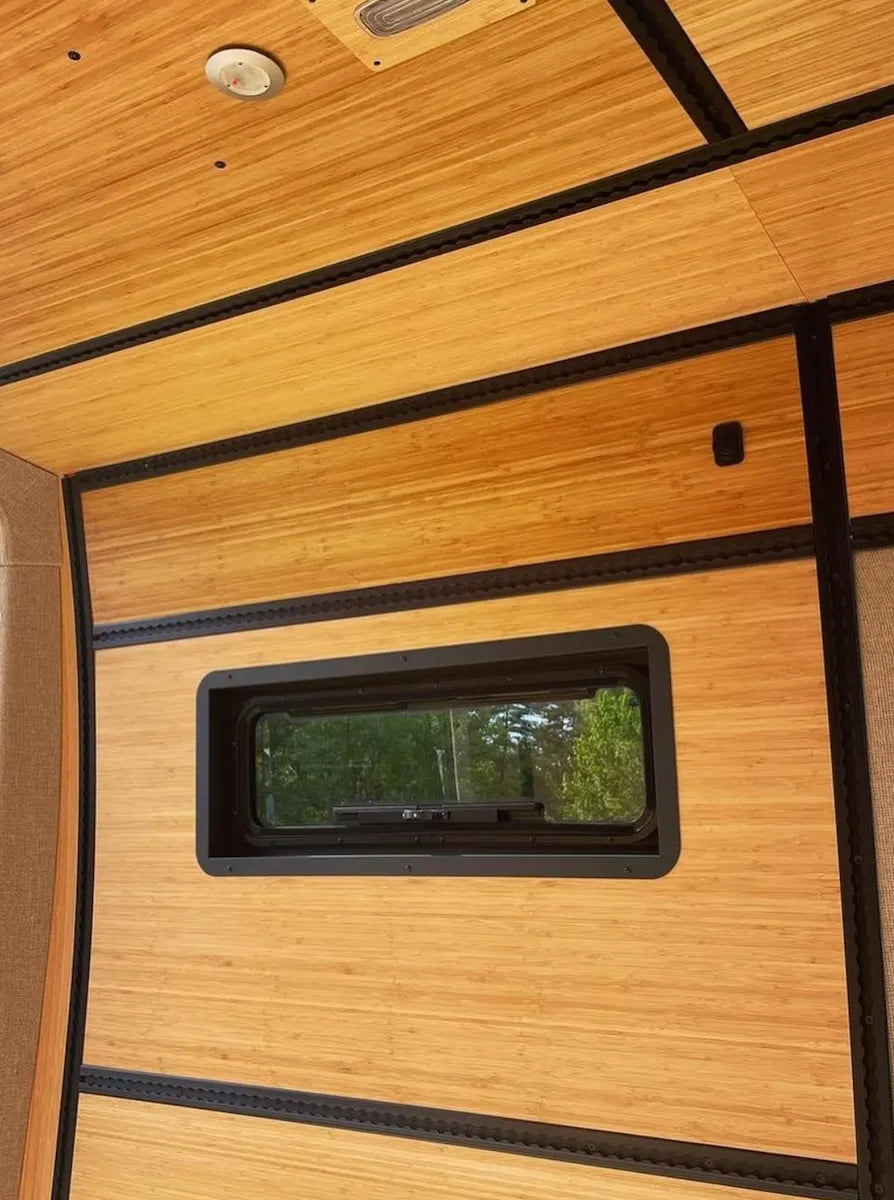 Close-up of an Adventure Wagon bamboo camper van wall panel with an integrated window and horizontal black L-Track.