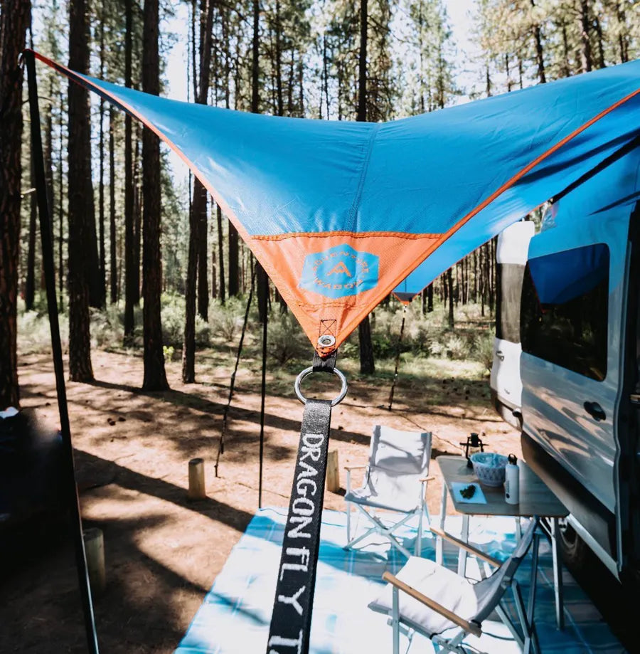Adventure Wagon camper van campsite setup with exterior awning, chairs and outdoor living area surrounded by forest.