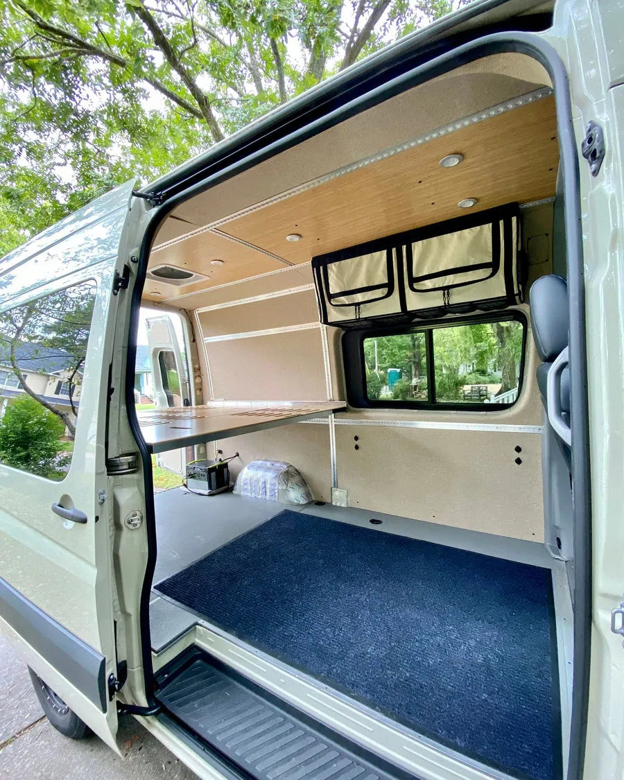 Adventure Wagon camper van interior with raised modular bed platform, bamboo ceiling, overhead storage and open gear space below.