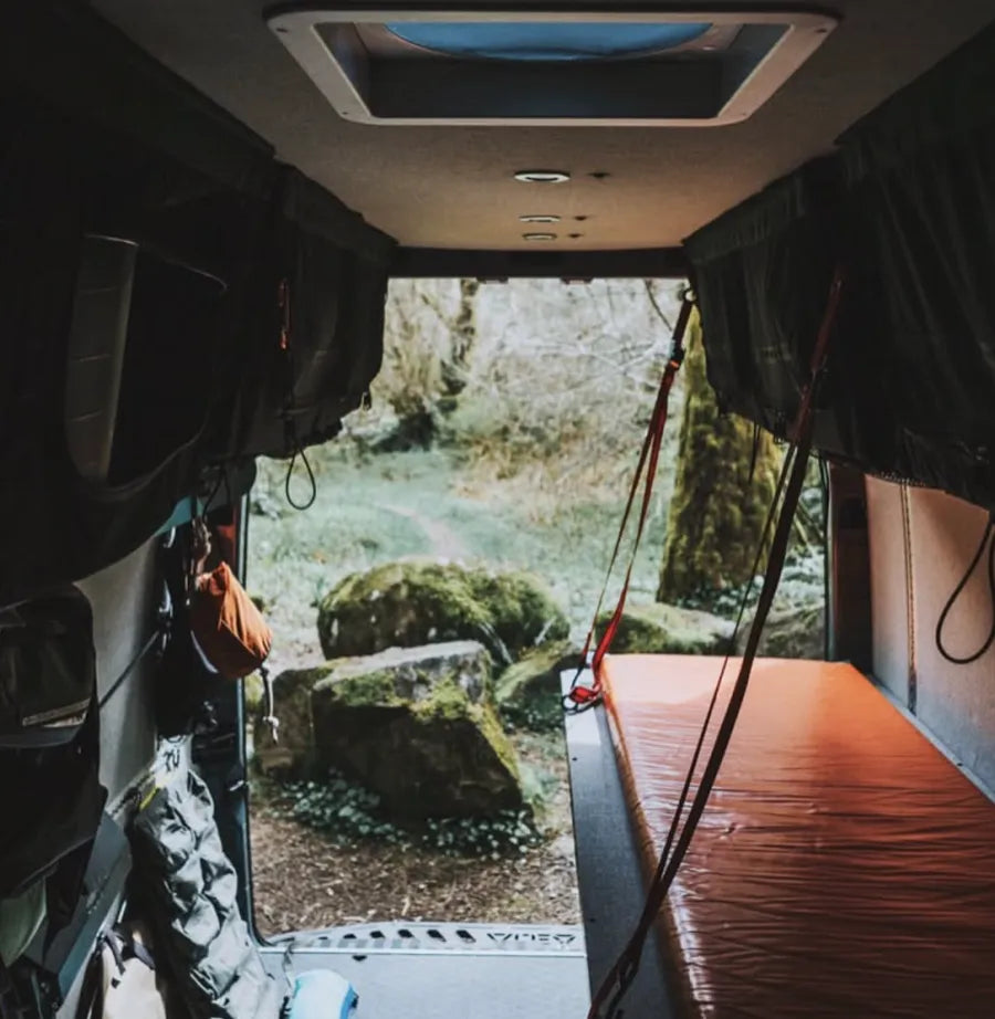 Adventure Wagon camper van bed platform and modular storage system framed by an open rear door with forest views outside.