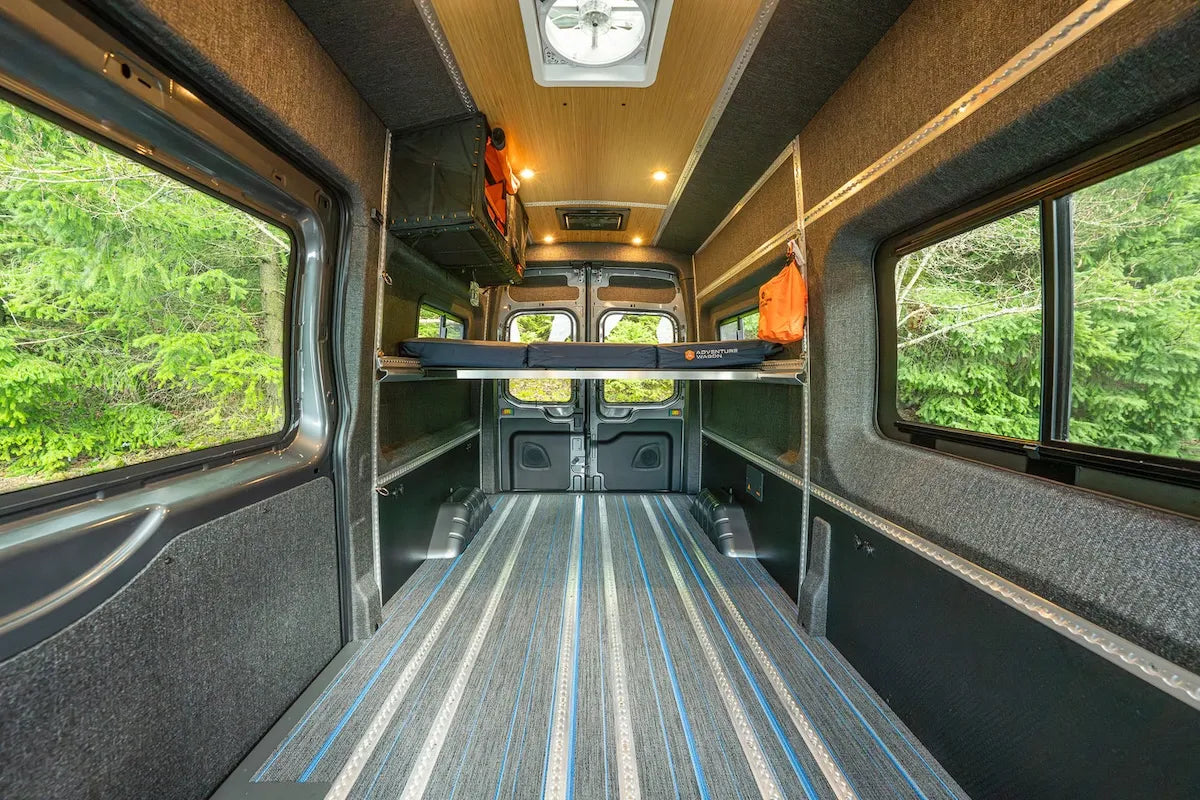 Adventure Wagon camper van interior with a raised modular bed platform, open floor space, finished walls and integrated L-Track.