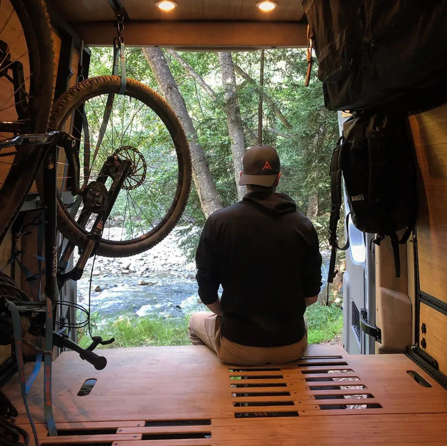 View from an Adventure Wagon camper van bed platform overlooking a wooded river through the open rear doors.