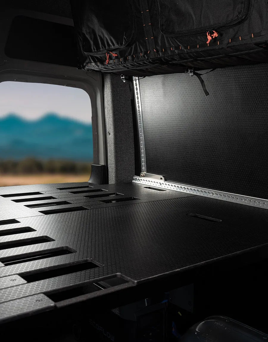 Close-up of Adventure Wagon modular bed platform and interior storage system with black textured panels and L-track mounting points.
