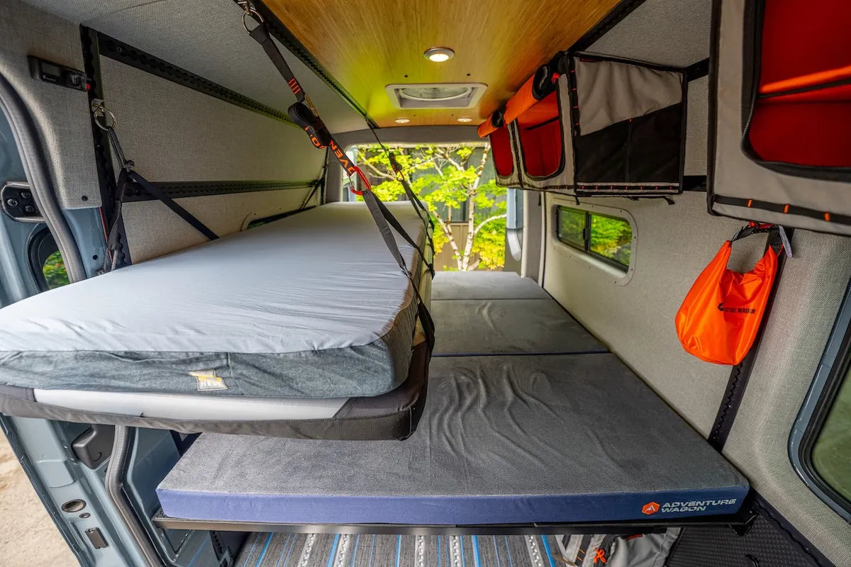 Adventure Wagon modular camper van bed system with suspended Soogan Bunk bed platform, Moab mattress, and surrounding overhead Mule Bag storage inside the finished interior.