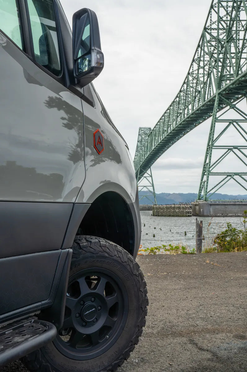 Close-up of an Adventure Wagon Mercedes Sprinter camper van exterior beside a large steel bridge.