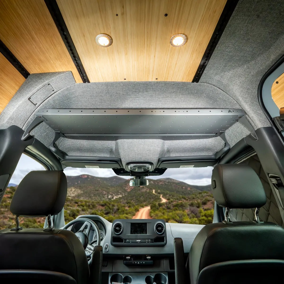 Adventure Wagon camper van cab with finished upholstered panels, bamboo ceiling, integrated lighting, and overhead storage above the front seats.