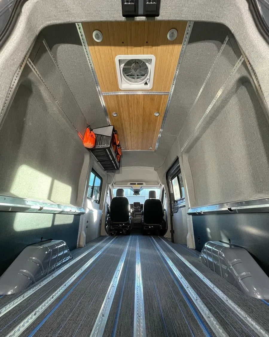 Empty Adventure Wagon camper van interior with upholstered wall panels, bamboo ceiling, roof fan and integrated floor L-track.