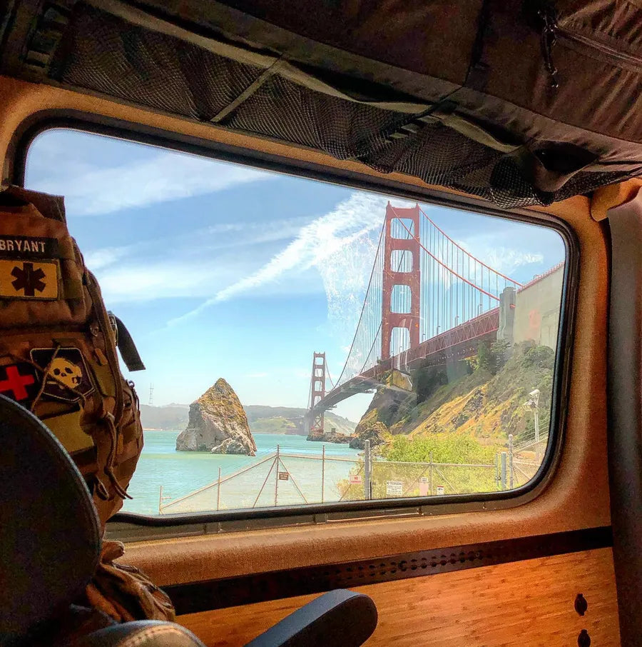 Golden Gate Bridge viewed through the side window of an Adventure Wagon camper van interior with bamboo wall paneling.