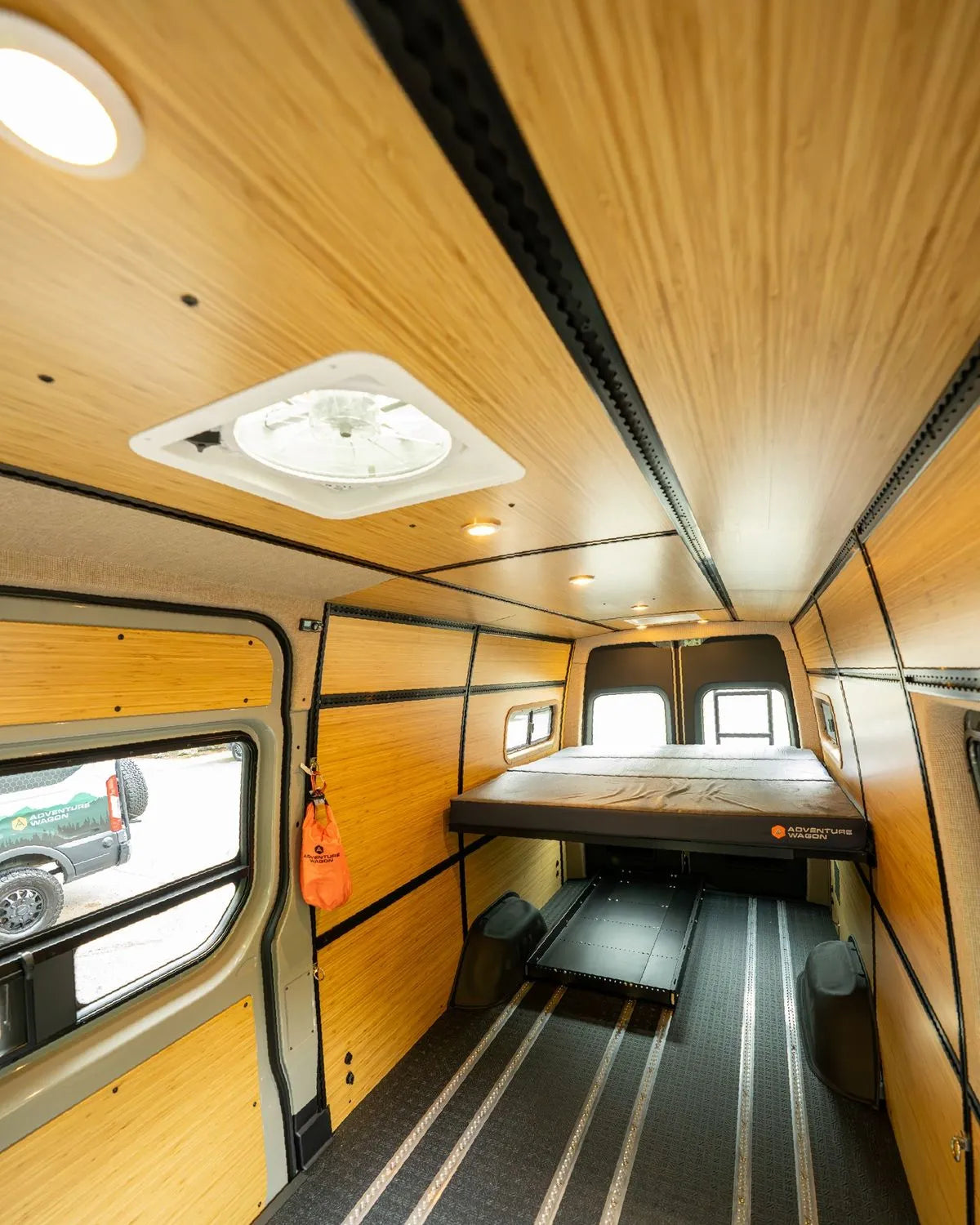 Adventure Wagon camper van interior with bamboo wall and ceiling panels, integrated L-Track, windows, and a raised modular bed platform.