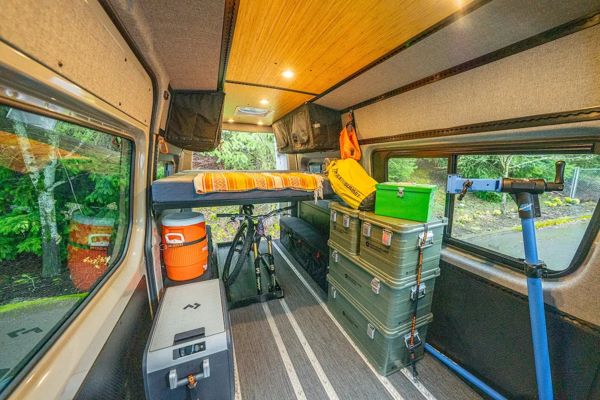 Adventure Wagon camper van interior configured as a flexible gear hauler with open floor space, overhead storage, fridge, and modular L-Track mounting.