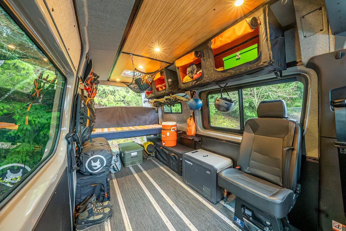 Adventure Wagon camper van interior with overhead Mule Bag storage, AUX boxes, fridge, open floor space, and integrated L-Track.