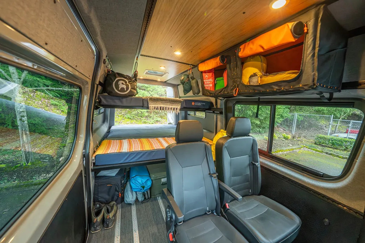 Adventure Wagon camper van interior configured with removable passenger seating, overhead gear storage, sleeping space, and integrated L-Track.