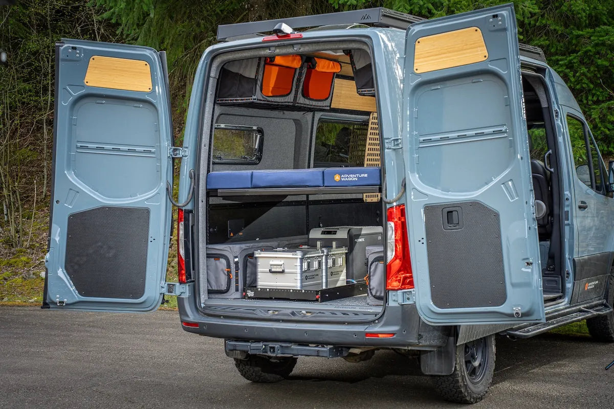 Rear cargo area of an Adventure Wagon camper van with organized gear storage, modular mule bags and aux boxes beneath the elevated bed platform.