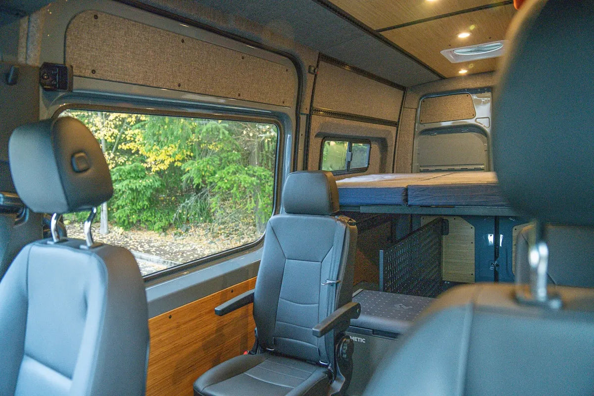 Adventure Wagon camper van interior configured with passenger seating, a raised traverse bed platform and flexible open space for travel and gear.