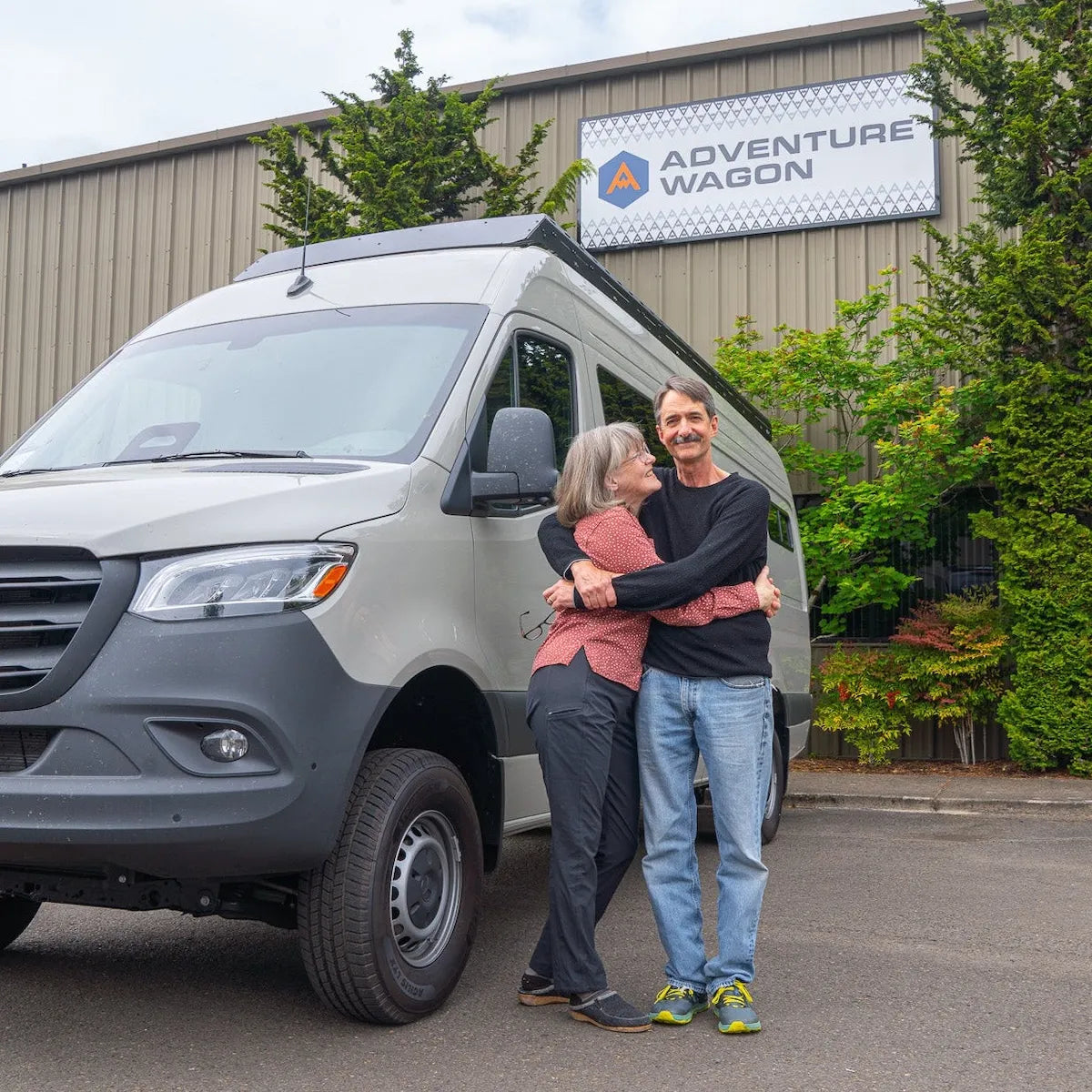 Adventure Wagon customers standing beside their completed Sprinter camper van outside the Adventure Wagon factory.