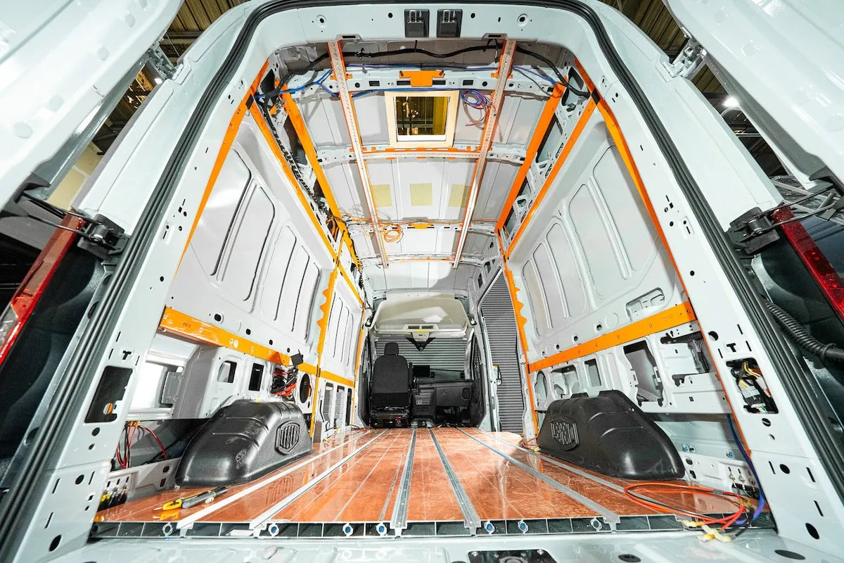 Adventure Wagon Factory Install showing orange A-Frame structural components installed inside the unfinished interior of a white camper van.