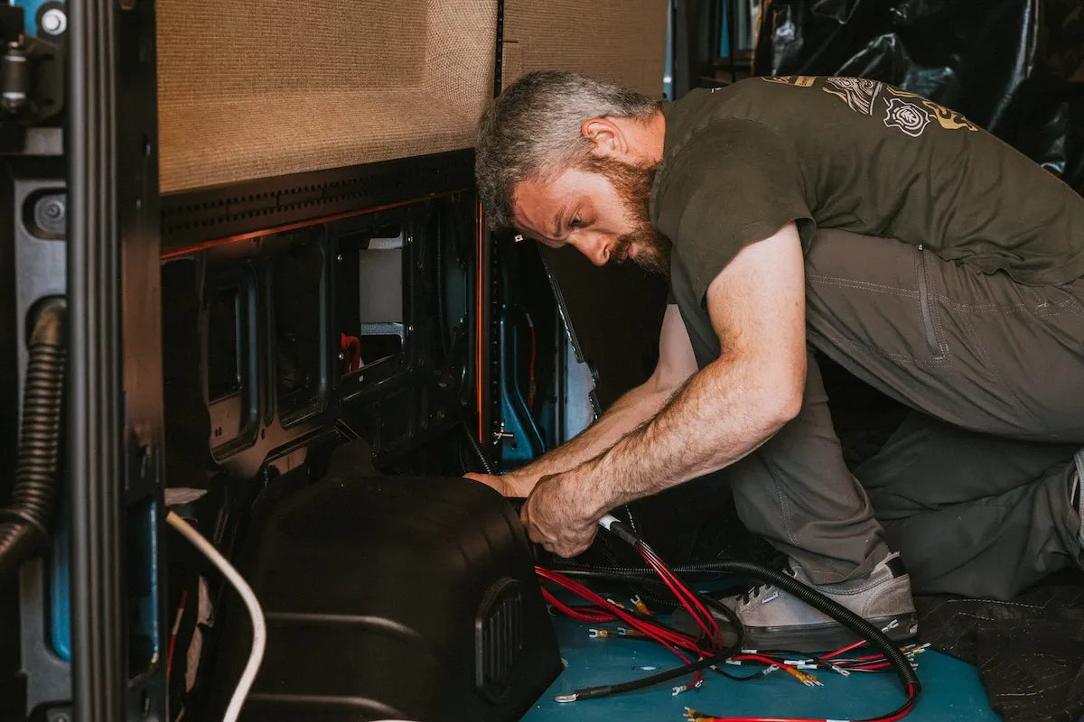 Adventure Wagon installer connecting electrical wiring and power components inside a camper van during the Factory Install process.