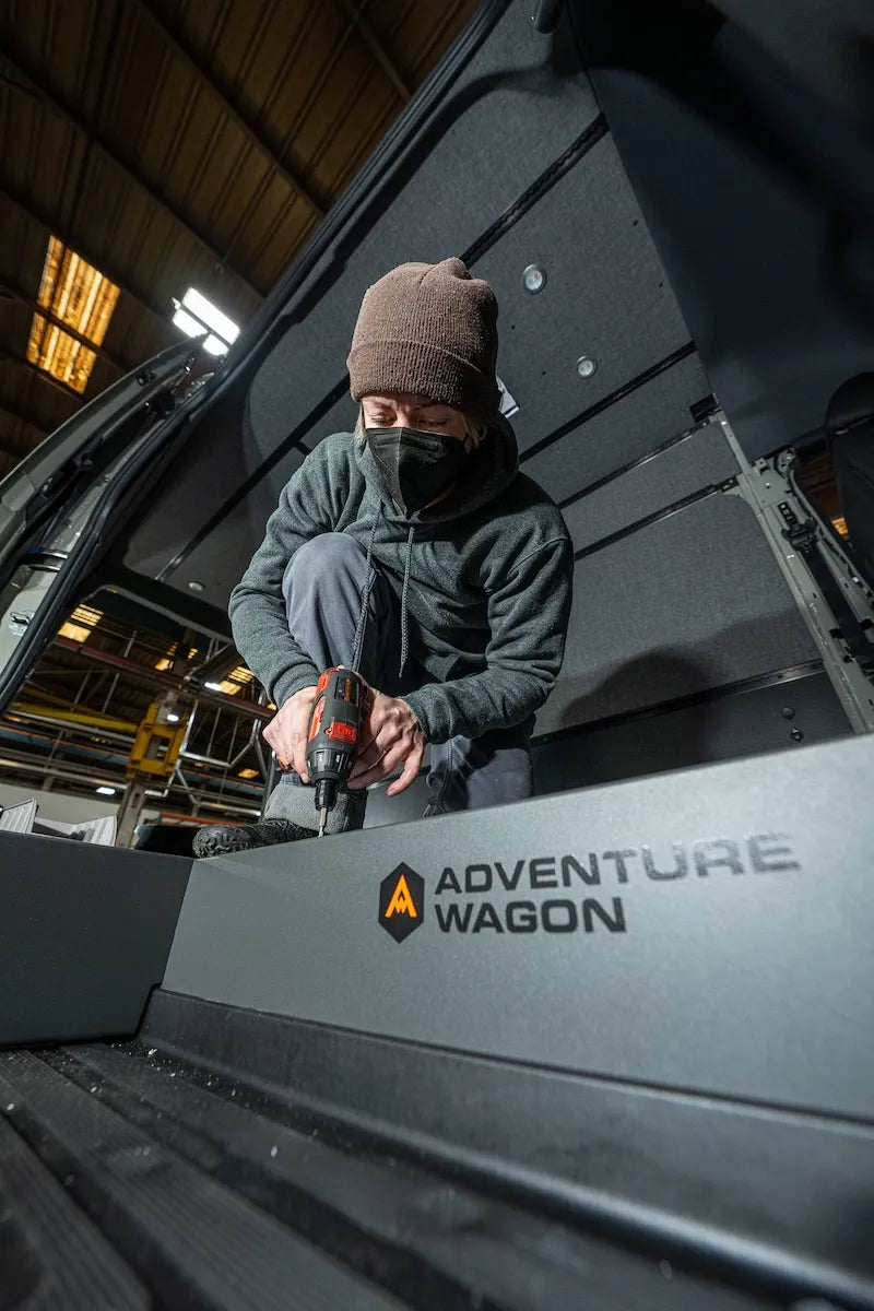 Adventure Wagon installer securing finished interior wall and ceiling panels inside a camper van during Factory Install.