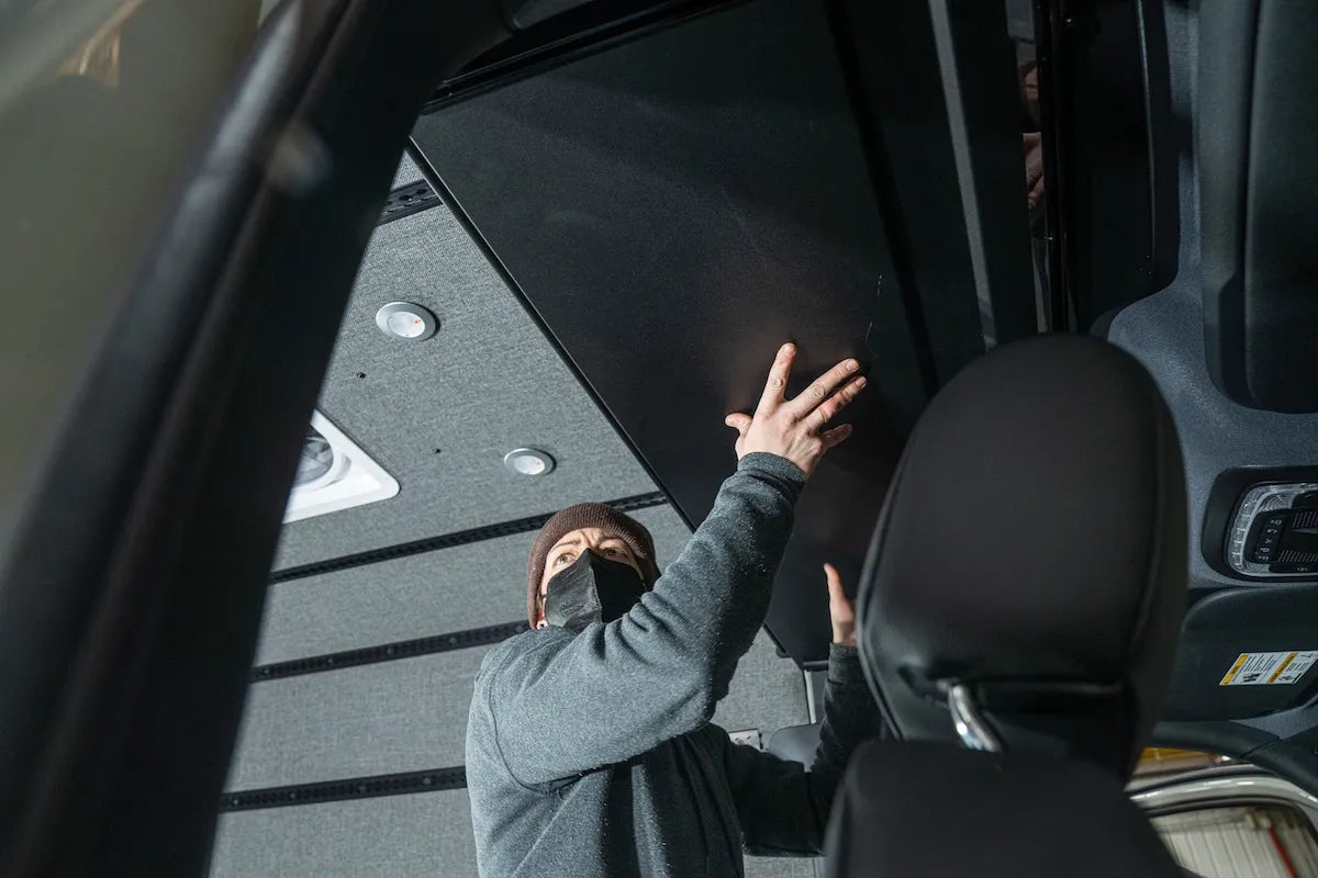 Adventure Wagon installer fitting an overhead interior panel above the front cabin inside a camper van during Factory Install.