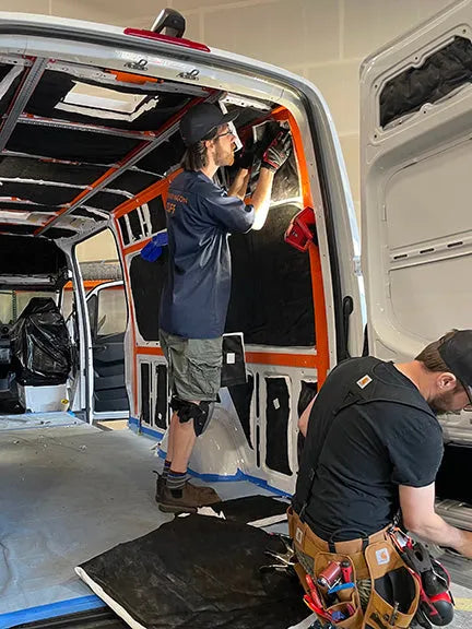Adventure Wagon Factory Install team working together inside a Sprinter van while installing insulation, wiring, framing, and interior components.