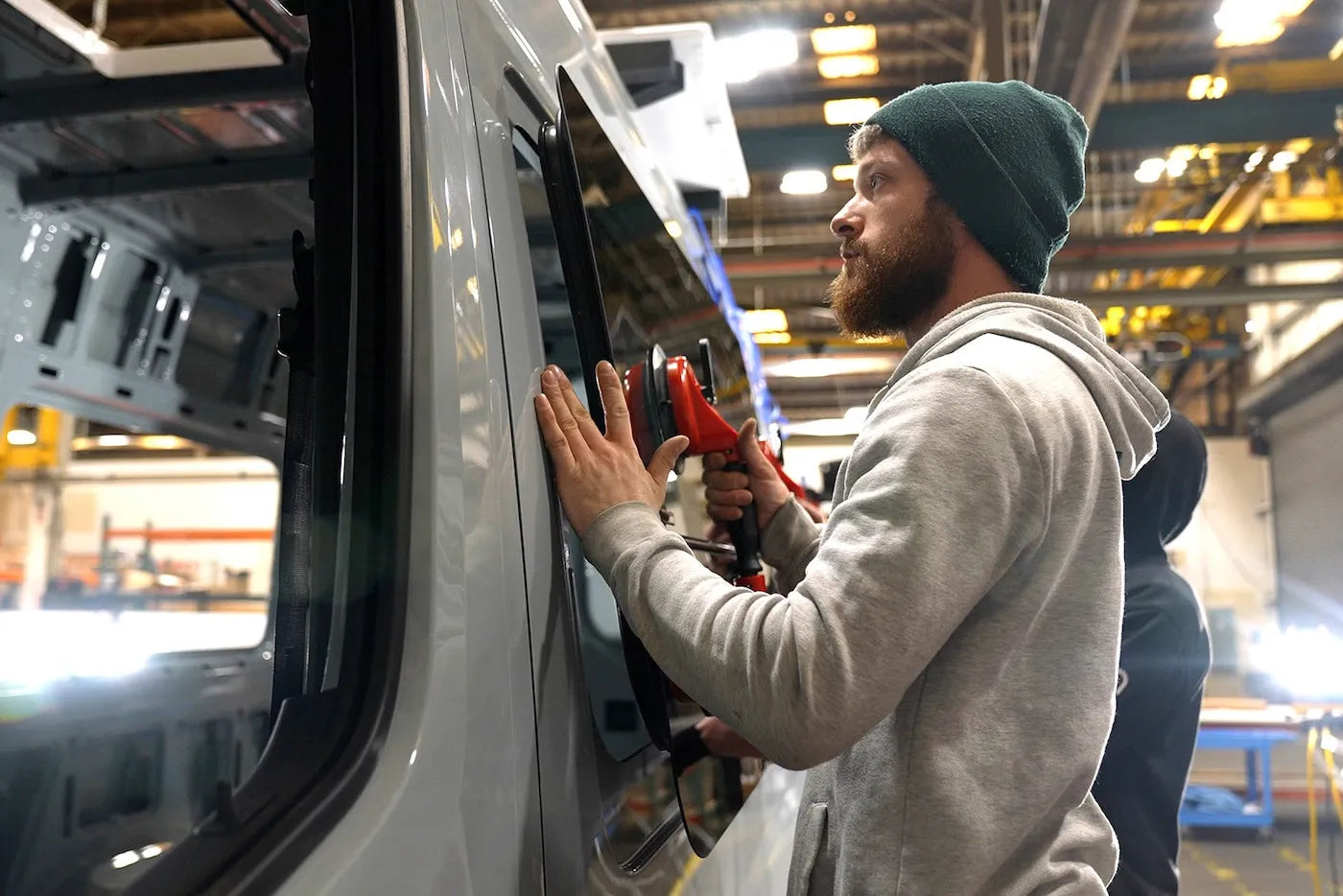 Adventure Wagon installer carefully positioning a camper van window into the side opening during the Factory Install process.