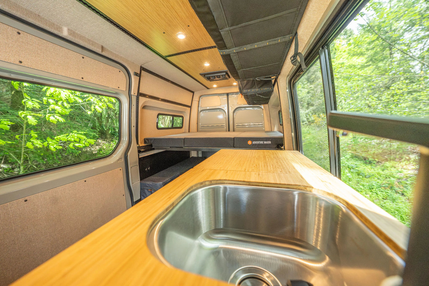 Adventure Wagon Guided Build 538 interior with bamboo galley sink, rear bed platform, windows, and overhead storage.