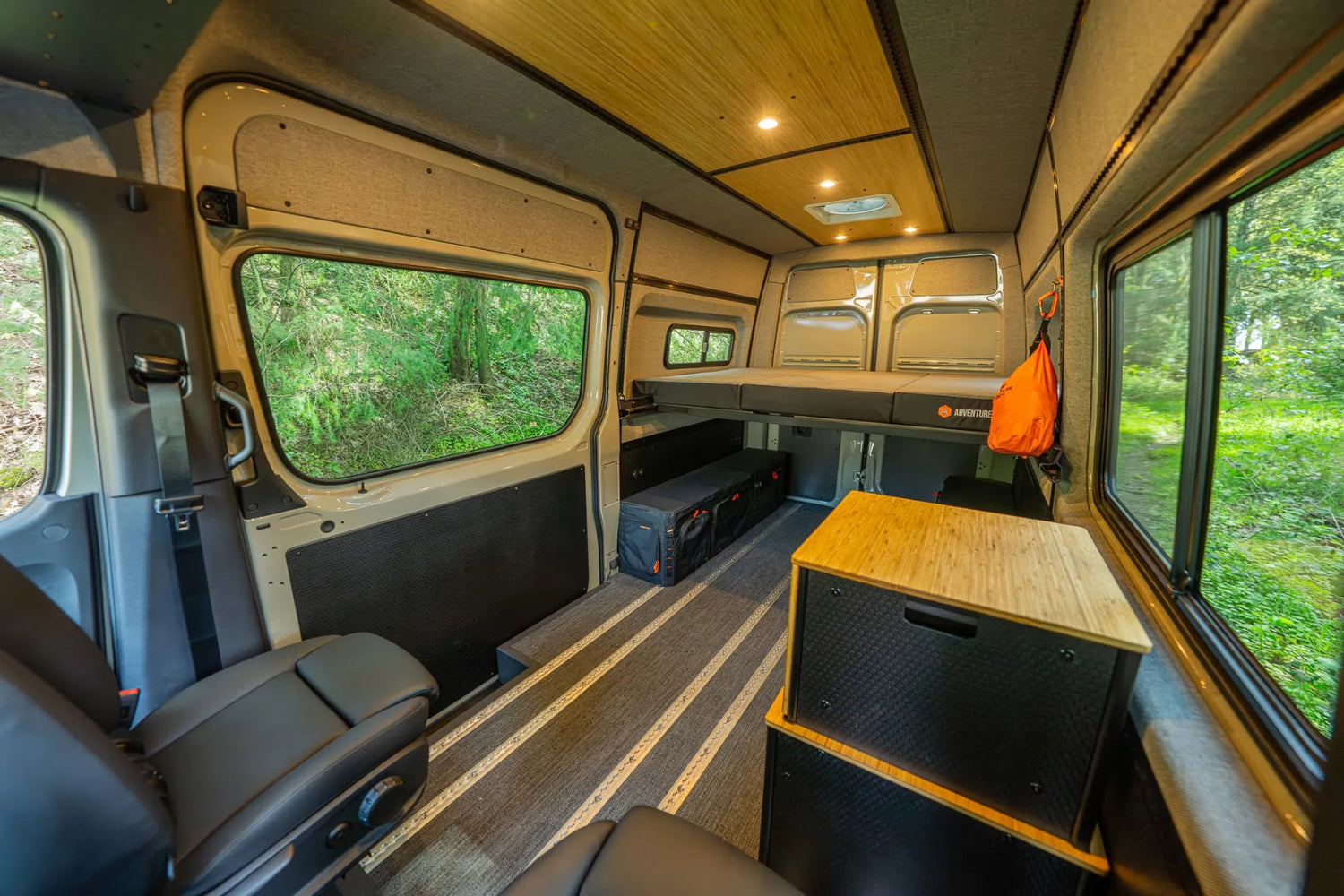 Adventure Wagon Guided Build 715 interior with modular platform cabinet, rear bed, L-track flooring, and camper van storage.