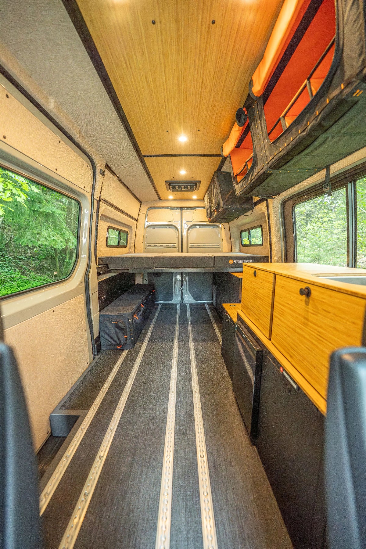 Adventure Wagon Guided Build 538 interior with bamboo cabinetry, galley storage, L-track flooring, bed platform, and overhead Mule Bags.
