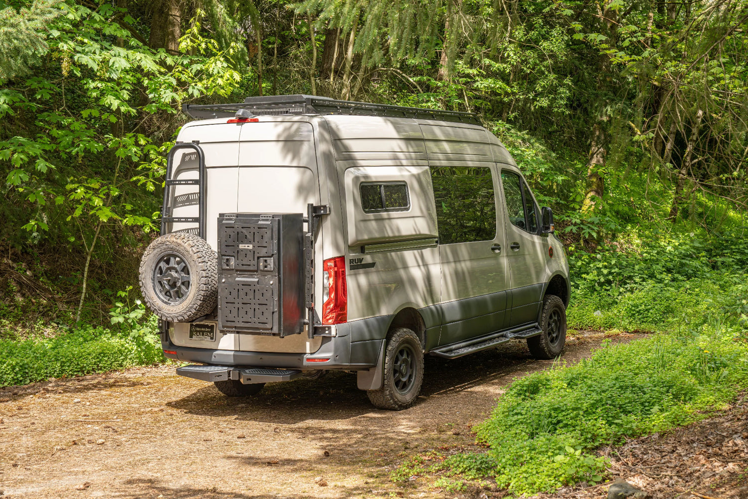 Adventure Wagon Guided Build 538 Mercedes Sprinter rear exterior parked in a forest with spare tire and exterior storage system.