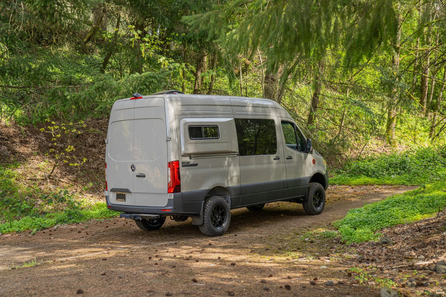 Adventure Wagon Guided Build 715 Mercedes Sprinter side exterior parked among trees.