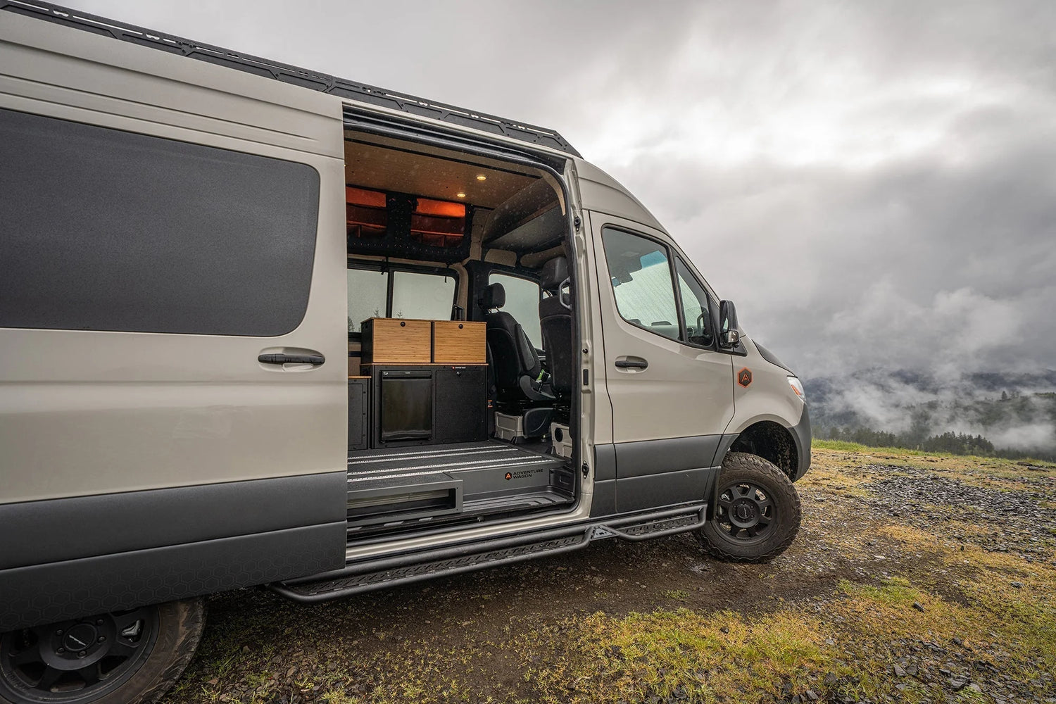 Adventure Wagon Guided Build Family of Four RUV 538 Mercedes-Benz Sprinter with the sliding door open, showing the Switchback Galley and interior storage at a misty mountain campsite.
