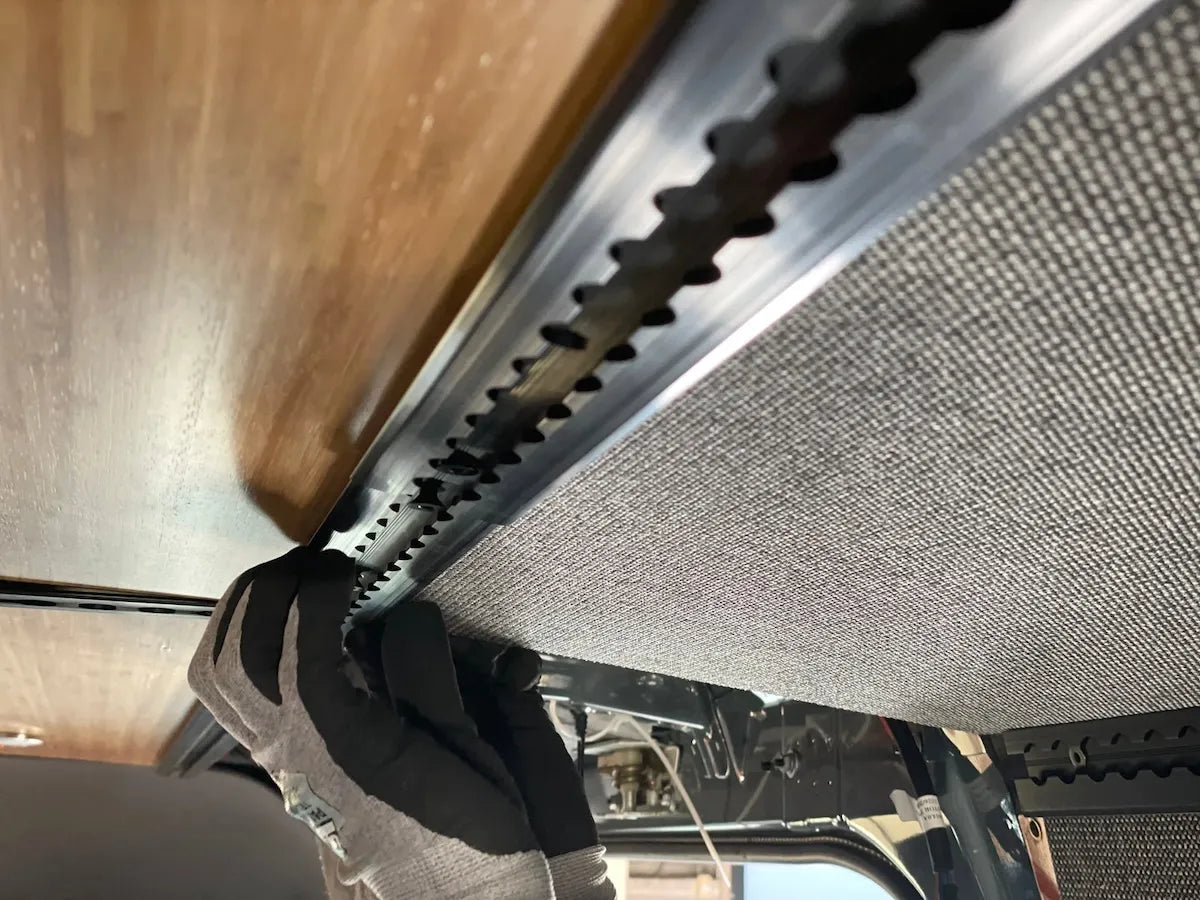 Close-up of Adventure Wagon interior L-Track being installed along an upholstered camper van wall beneath a bamboo ceiling panel.