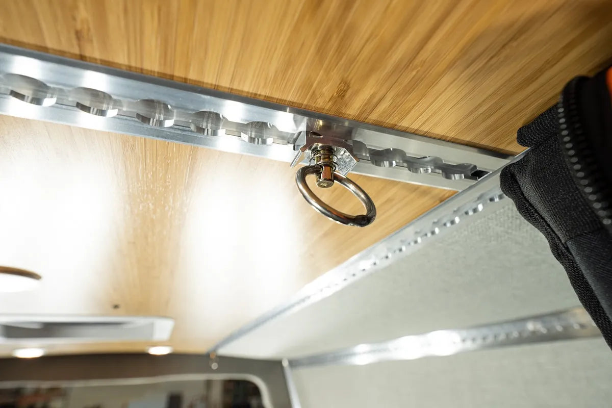 Close-up of an Adventure Wagon L-Track tie-down ring mounted to ceiling track for securing gear and attaching modular camper van accessories.