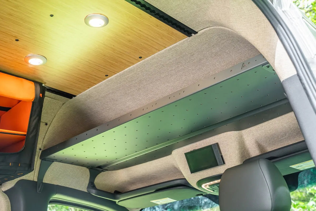 Close-up of the Adventure Wagon overhead cab shelf mounted above the front seats and integrated into the upholstered camper van headliner.