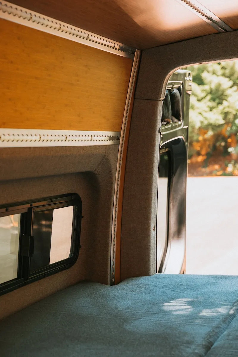 Adventure Wagon camper van interior viewed through the rear doors with bamboo wall panels and a Traverse bed platform.
