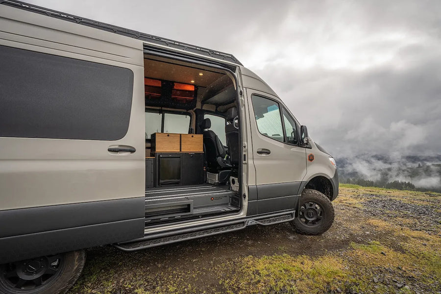 Adventure Wagon RUV Sprinter camper van parked at a misty mountain overlook with the sliding side door open, revealing the modular interior and galley.