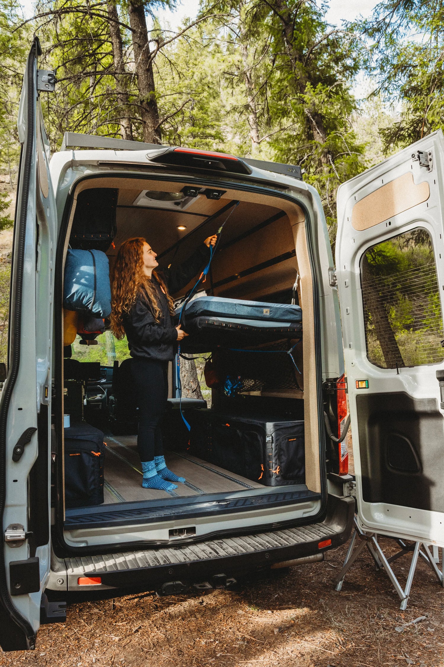 Solo traveler adjusting the suspended Soogan Bunk inside the Adventure Wagon Solo Nomad camper van.
