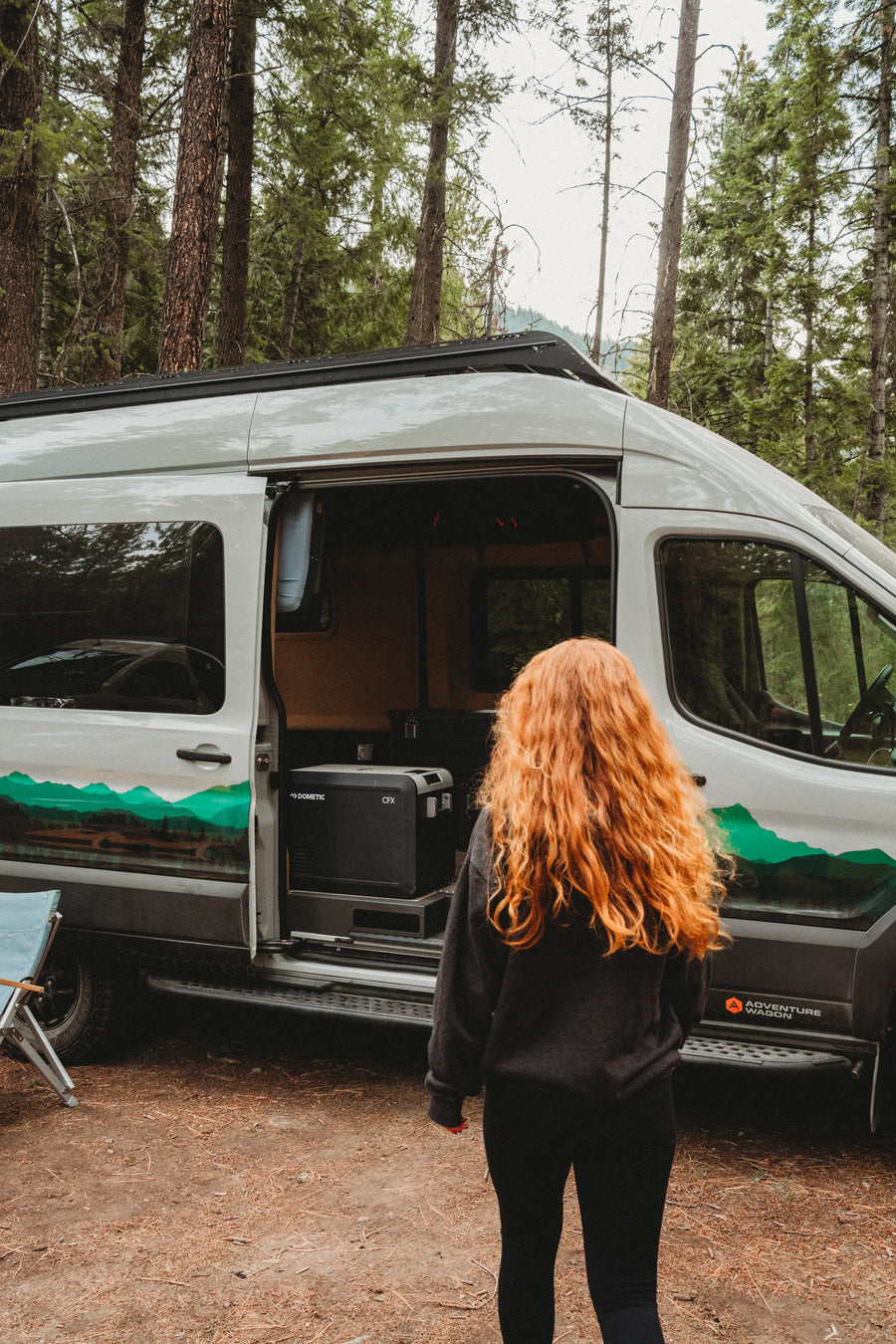 Solo traveler beside the open van door with a Dometic CFX fridge in the Adventure Wagon Solo Nomad.