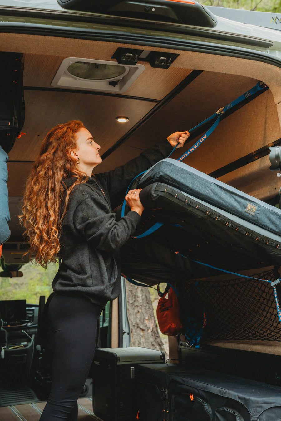 Solo traveler adjusting the straps on the Soogan Bunk inside the Adventure Wagon Solo Nomad camper van.