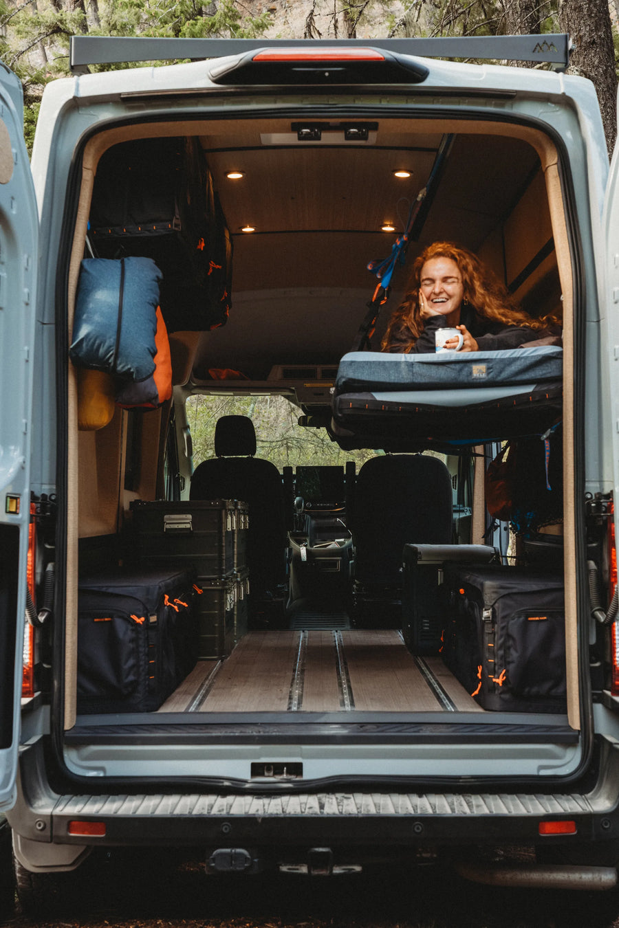 Solo traveler relaxing with a mug in the Soogan Bunk inside the Adventure Wagon Solo Nomad van.