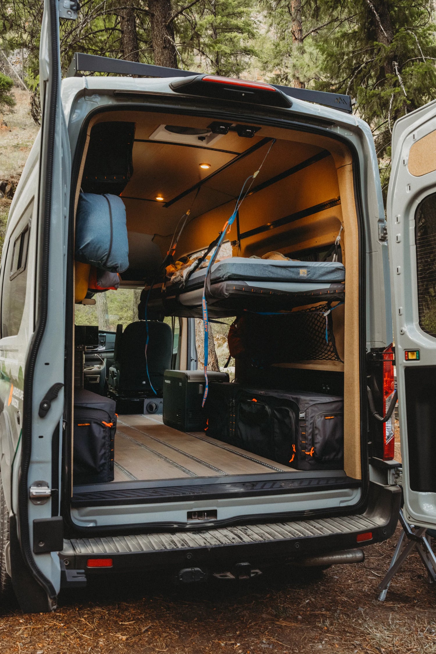 Adventure Wagon Solo Nomad camper van interior with rear doors open, suspended Soogan bunk, and gear storage.